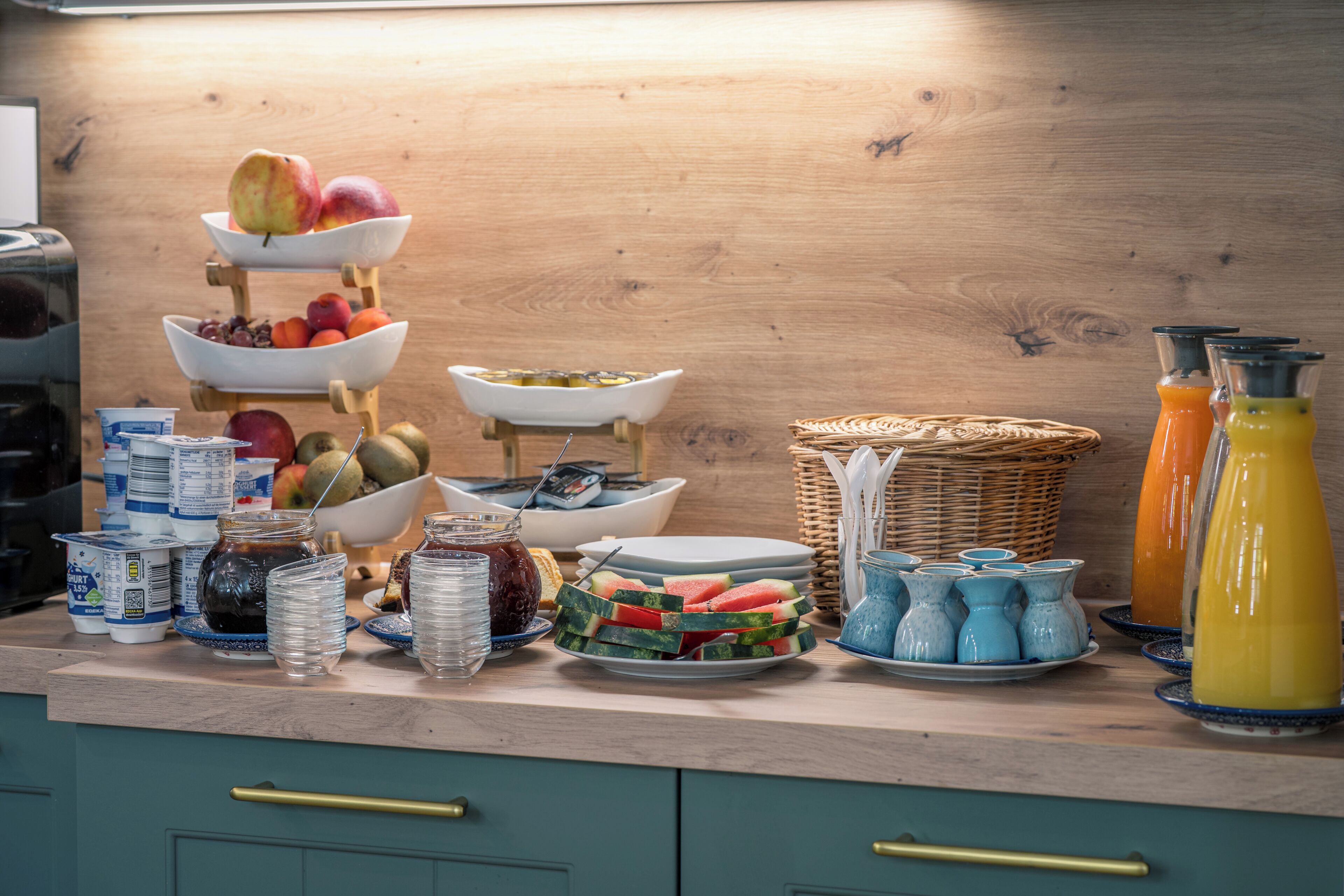 Un bufé de desayuno con diversas frutas, bebidas y recipientes sobre una encimera de madera.