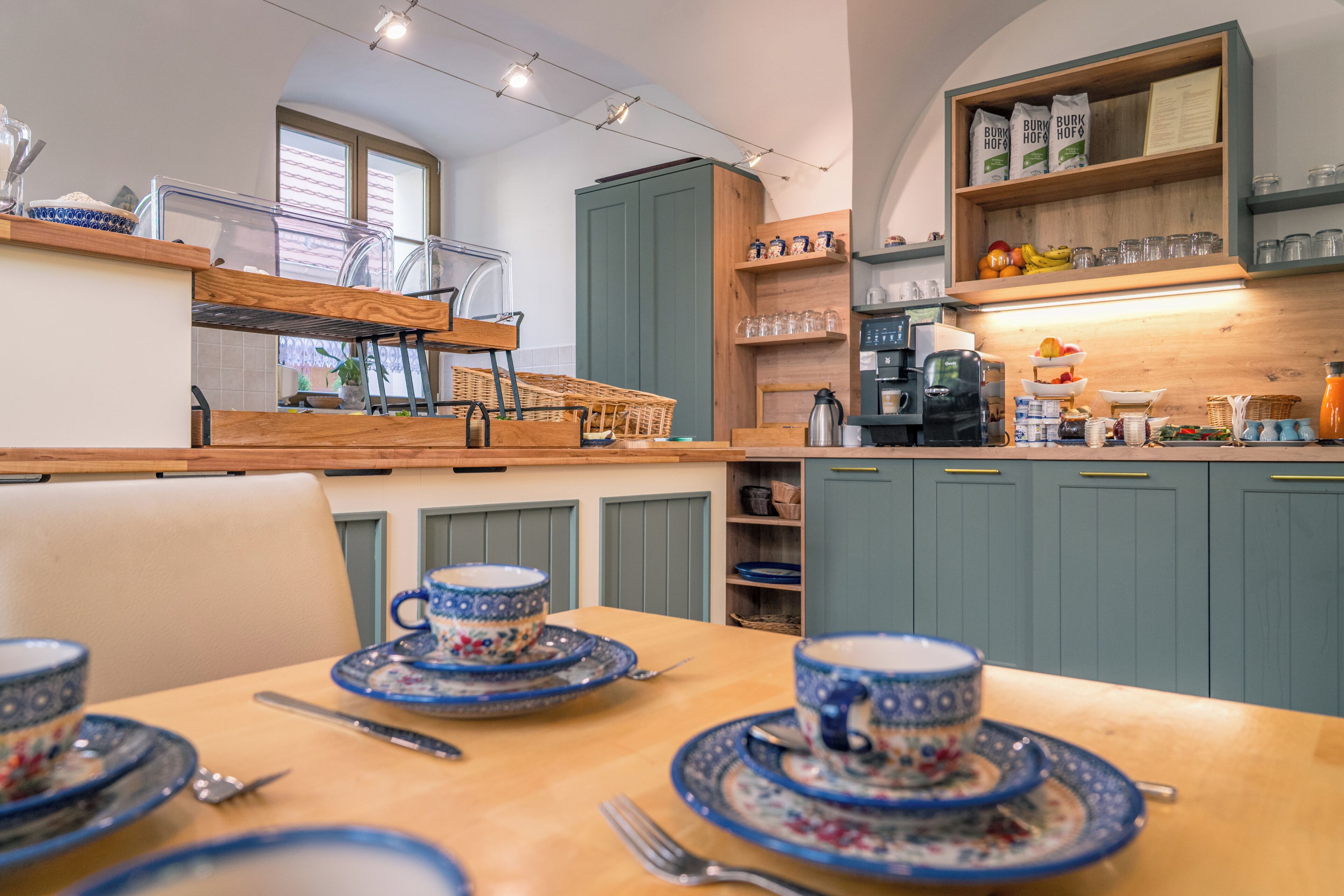 Een keuken met een eettafel voor vier personen, een koffieapparaat en een plank met keukengerei.