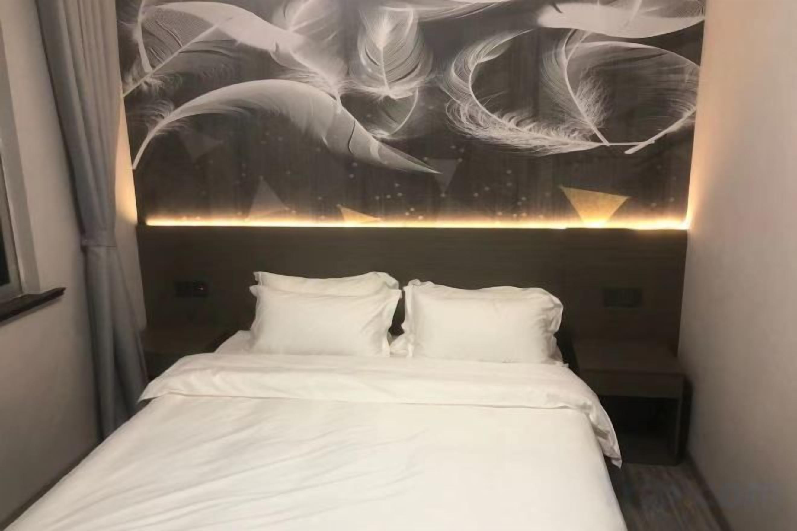 A hotel room with a bed, a headboard with a feather-like design, and a nightstand.