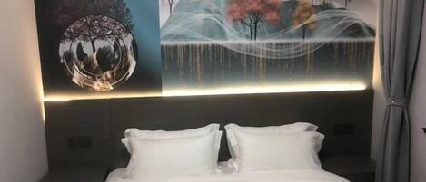 A bed with white bedding, a headboard with a lighted panel, and a wall with a nature-themed mural.