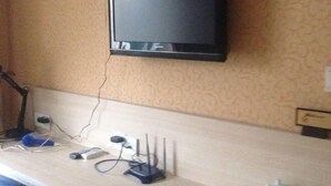 A room with a mounted flat-screen TV, a desk with a computer, a lamp, and a power strip with cables. - Shanghai Evening Fenglin Hotel (Shanghai)