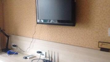 Ein an der Wand befestigter Fernseher, eine Steckdose und ein Schreibtisch mit Computer und verschiedenen Kabeln.