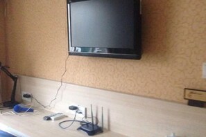 Un téléviseur fixé au mur, une prise de courant et un bureau avec un ordinateur et divers câbles.