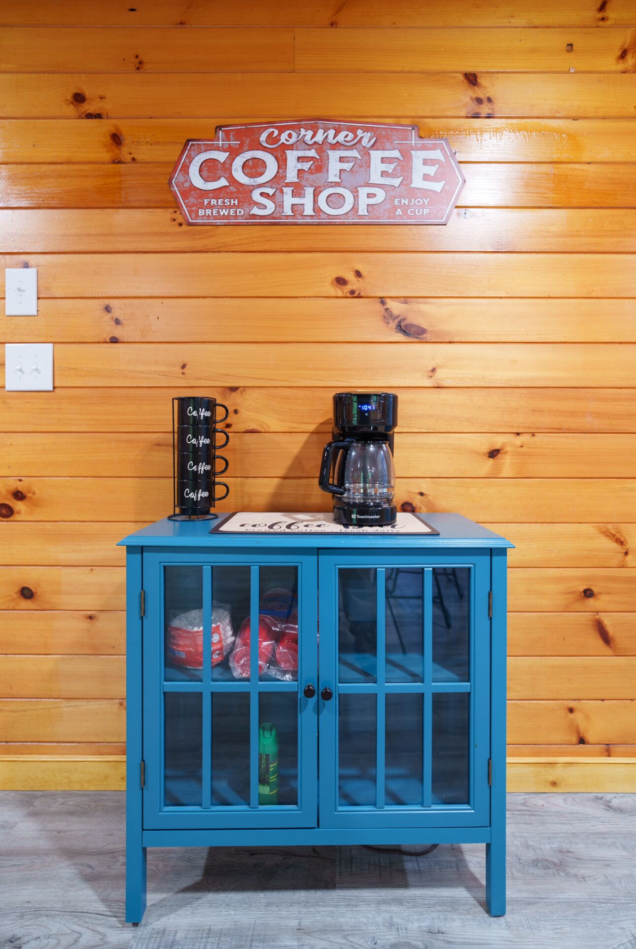 Een blauwe kast met glazen deuren, een koffiezetapparaat en een bord erboven met de tekst 'Corner Coffee Shop'.