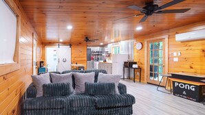 A cozy cabin interior with a plush sofa, wooden walls, a ceiling fan, and a ping pong table.