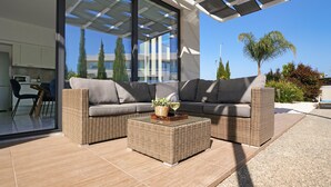 A modern outdoor living area with a sectional sofa, two square wicker coffee tables, and a glass-top table with a wine glass and a plant. - Villa Camellia - 3bed Bungalow large pool (Protaras)