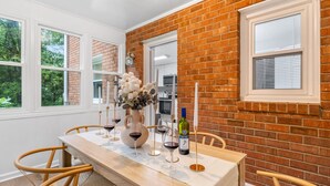 A dining area with a brick wall, white-framed windows, and a wooden table set with wine glasses and a vase of flowers. - 4BR 50-Acre Ridge Retreat | Nature & Fire Pit (Greensboro)