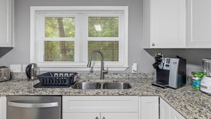 A kitchen with a granite countertop, a stainless steel sink, a coffee maker, and a window with blinds. - 4BR 50-Acre Ridge Retreat | Nature & Fire Pit (Greensboro)