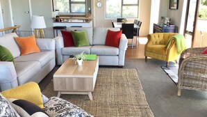 Una sala de estar moderna con un sofá gris, una mesa de centro y un sillón amarillo. Hay una zona de cocina con un fregadero y una mesa de comedor.