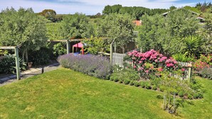 Un jardín bien cuidado con diversas plantas y flores, una valla de madera y una estructura de pérgola.