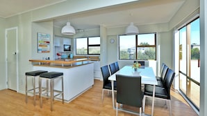 Una cocina moderna con una isla central, taburetes de bar y un comedor con mesa blanca y sillas negras.