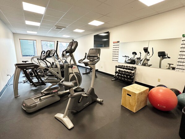 Ein Fitnessraum mit Laufbändern, Crosstrainern, einem Gewichtständer und Trainingsbällen.
