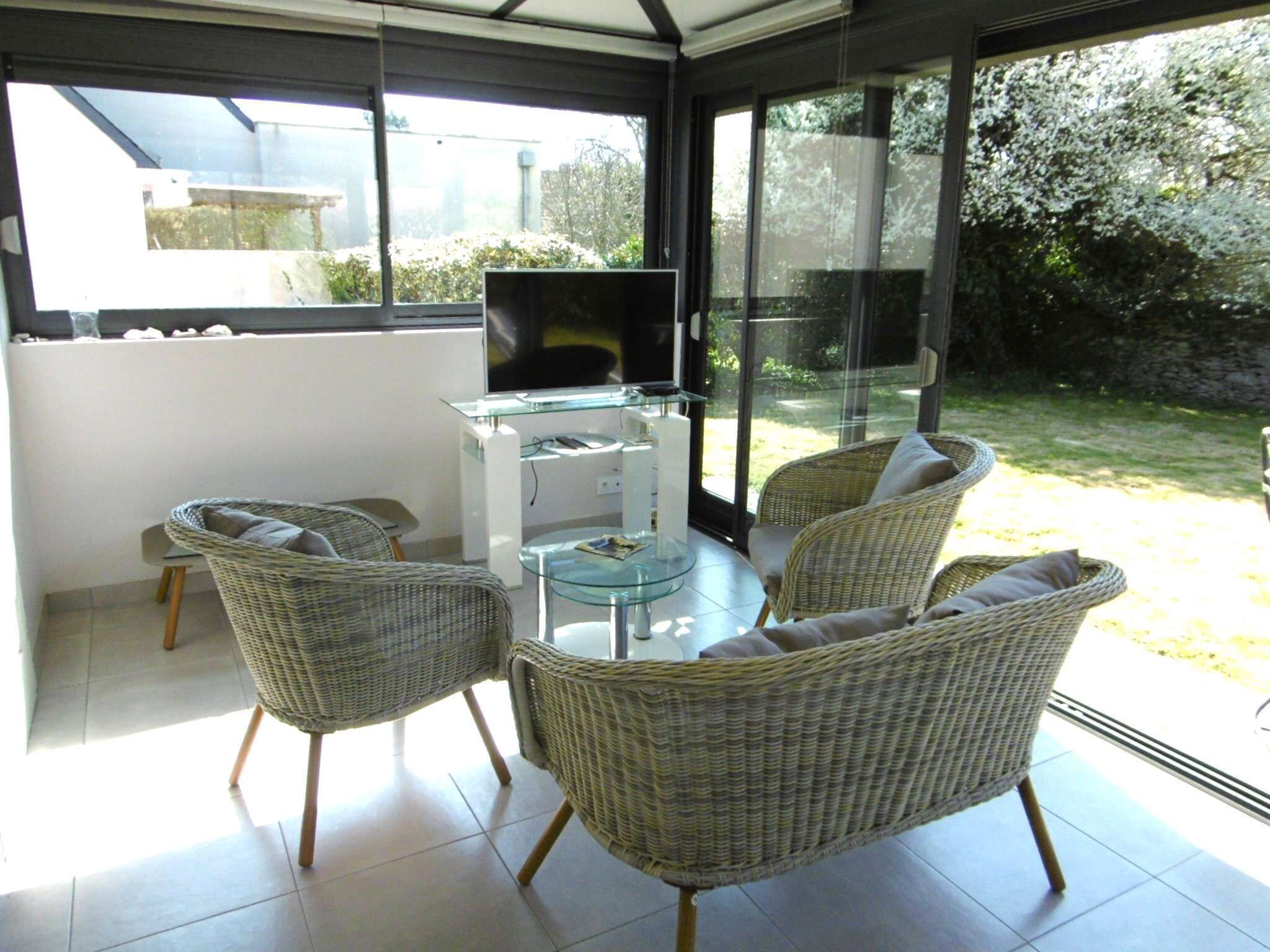 Een zonnig terras met rieten meubels, een glazen tafel en een televisie op een witte kast.