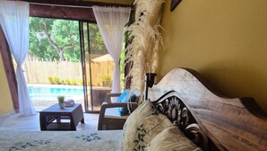 A bedroom with a bed, a small table, and a view of an outdoor area with a pool.