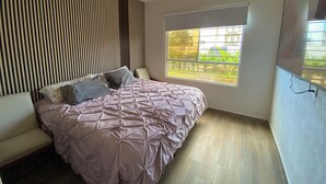 Ein modernes Schlafzimmer mit einem großen Bett, einem Fenster mit Blick auf Grünflächen und einer Wandgestaltung mit Lamellen.