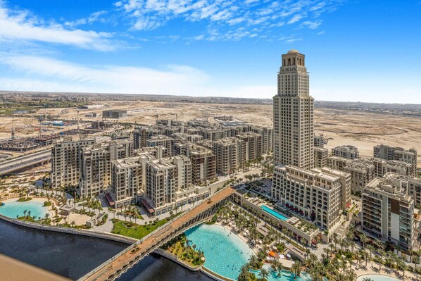 A high-rise hotel with a central tower, multiple surrounding buildings, and a large swimming pool area with palm trees.