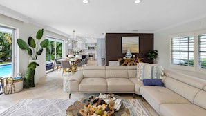 A spacious living area with a beige sectional sofa, a coffee table with decorative items, and a view of a kitchen and dining area. - Chic 3 BR Villa with Private Pool – Fort Lauderdale (Fort Lauderdale)