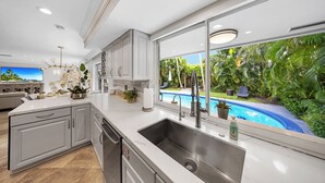 A modern kitchen with a large window overlooking a pool, built-in cabinets, and a central island. - Chic 3 BR Villa with Private Pool – Fort Lauderdale (Fort Lauderdale)