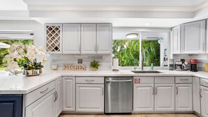 A modern kitchen with white cabinets, a stainless steel dishwasher, and a view of lush greenery outside. - Chic 3 BR Villa with Private Pool – Fort Lauderdale (Fort Lauderdale)