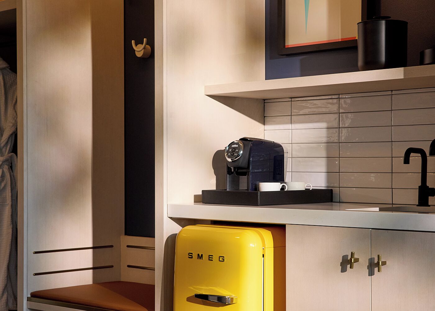 A modern bathroom with a coffee machine, a yellow Smeg sink, and a towel rack.