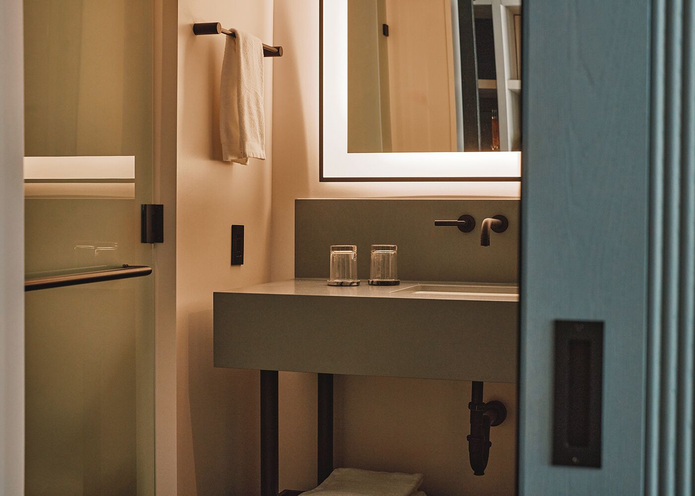 A modern bathroom with a large mirror, a sink, and two glass bottles on the counter.