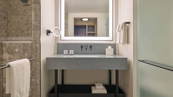A modern bathroom with a grey sink, a large mirror, a towel rack, and a shower area.