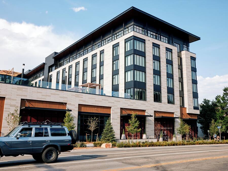 A modern building with multiple floors, large windows, and a parking area with a blue SUV.