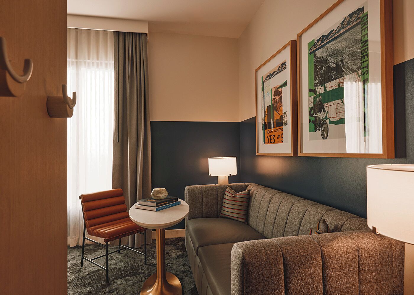 Habitación de hotel con sofá, una pequeña mesa redonda con libros, una silla, una lámpara y dos cuadros en la pared.