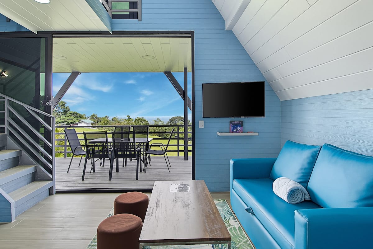 Un interior moderno con un sofá azul, una mesa de madera y un televisor montado en la pared.