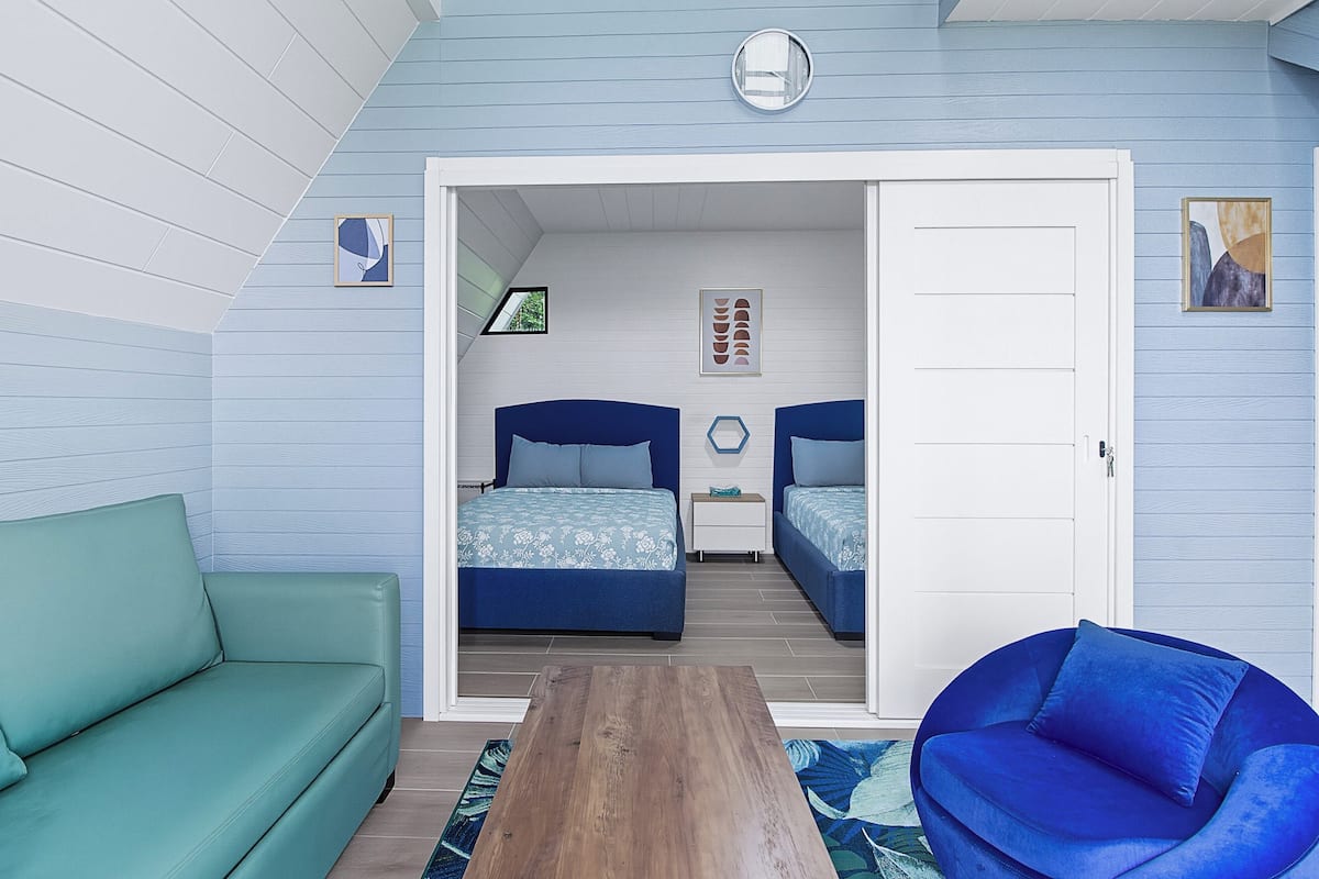 Un dormitorio con dos camas, un sofá verde, una silla azul y una mesa de madera.