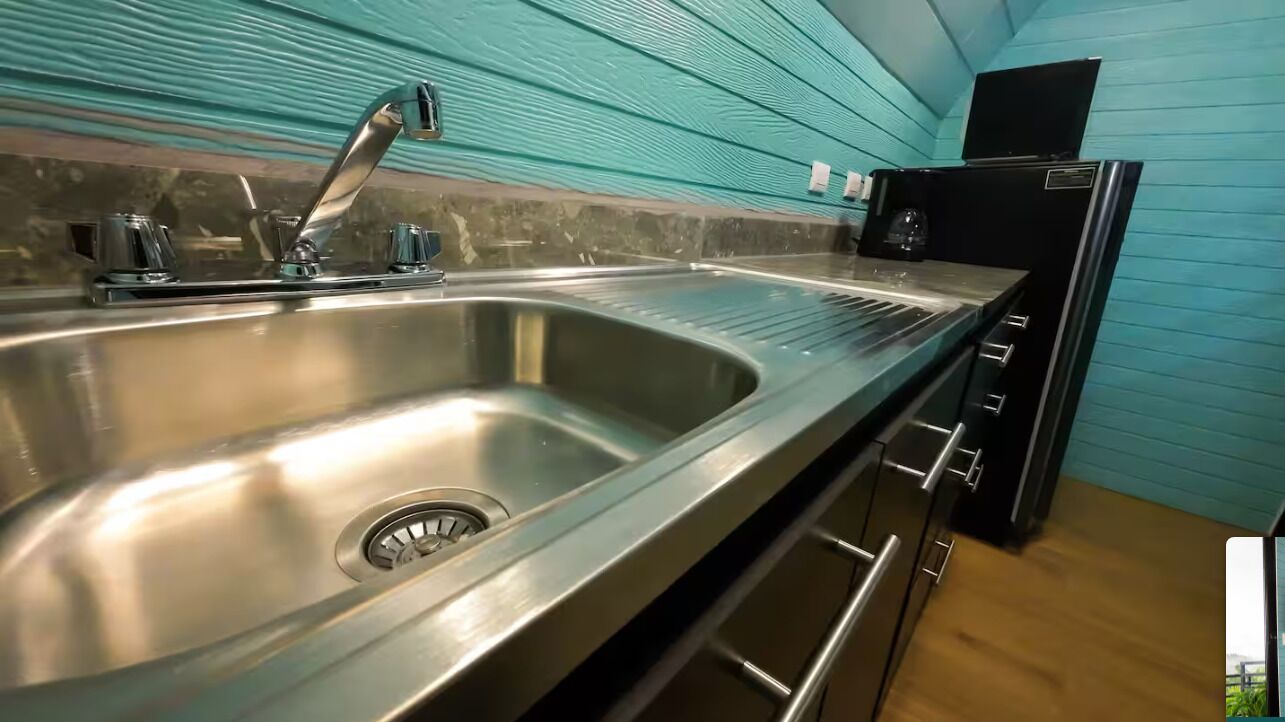 A kitchen with a stainless steel sink, a black refrigerator, and a teal-colored wall.