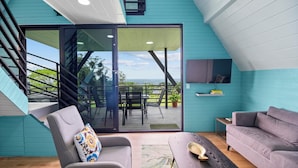 A modern interior with a grey sofa, a wooden coffee table, and a view through a glass door to an outdoor deck. - Junglo Resort and Spa (Peñas Blancas)