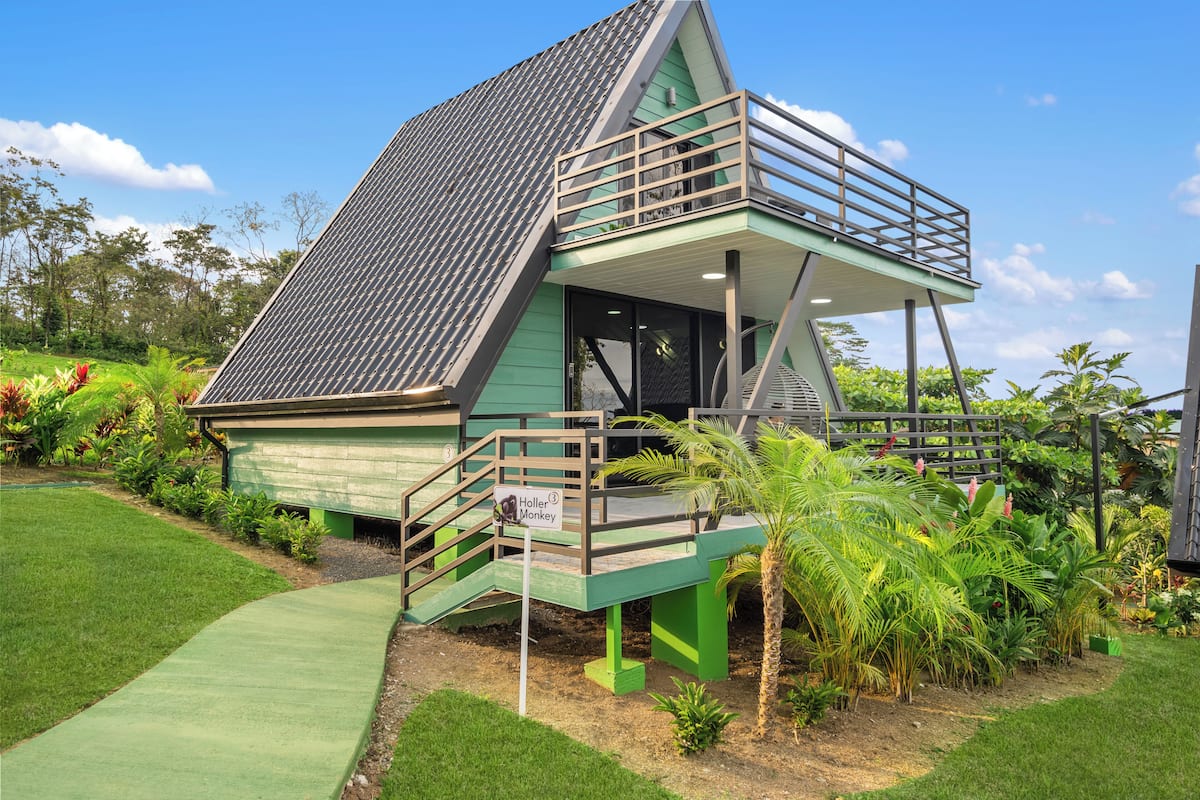 Una casa verde con techo inclinado, un balcón y una escalera que conduce a la entrada.