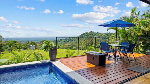 A poolside area with a wooden deck, a table with chairs, and a blue umbrella. - Junglo Resort and Spa (Peñas Blancas)