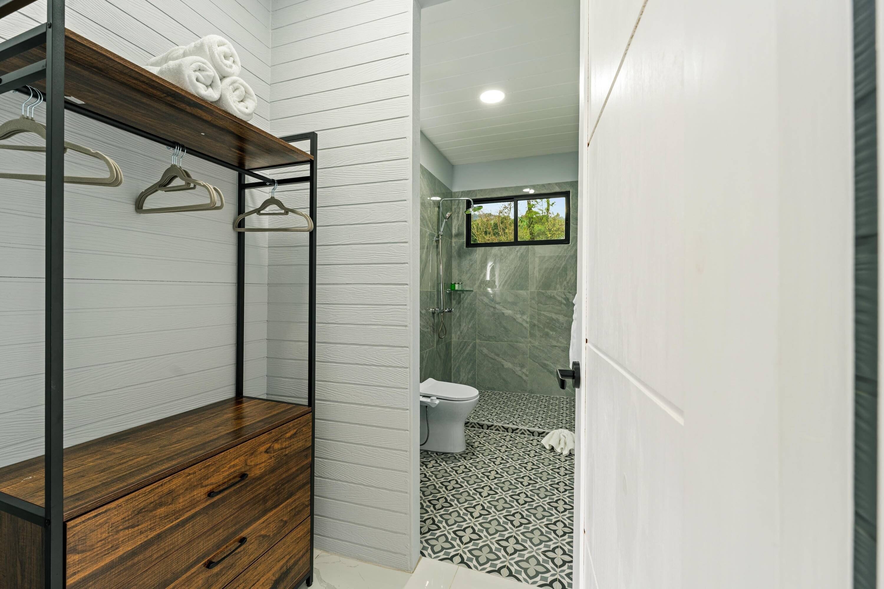 A bathroom with a shower, toilet, and a wooden bench.