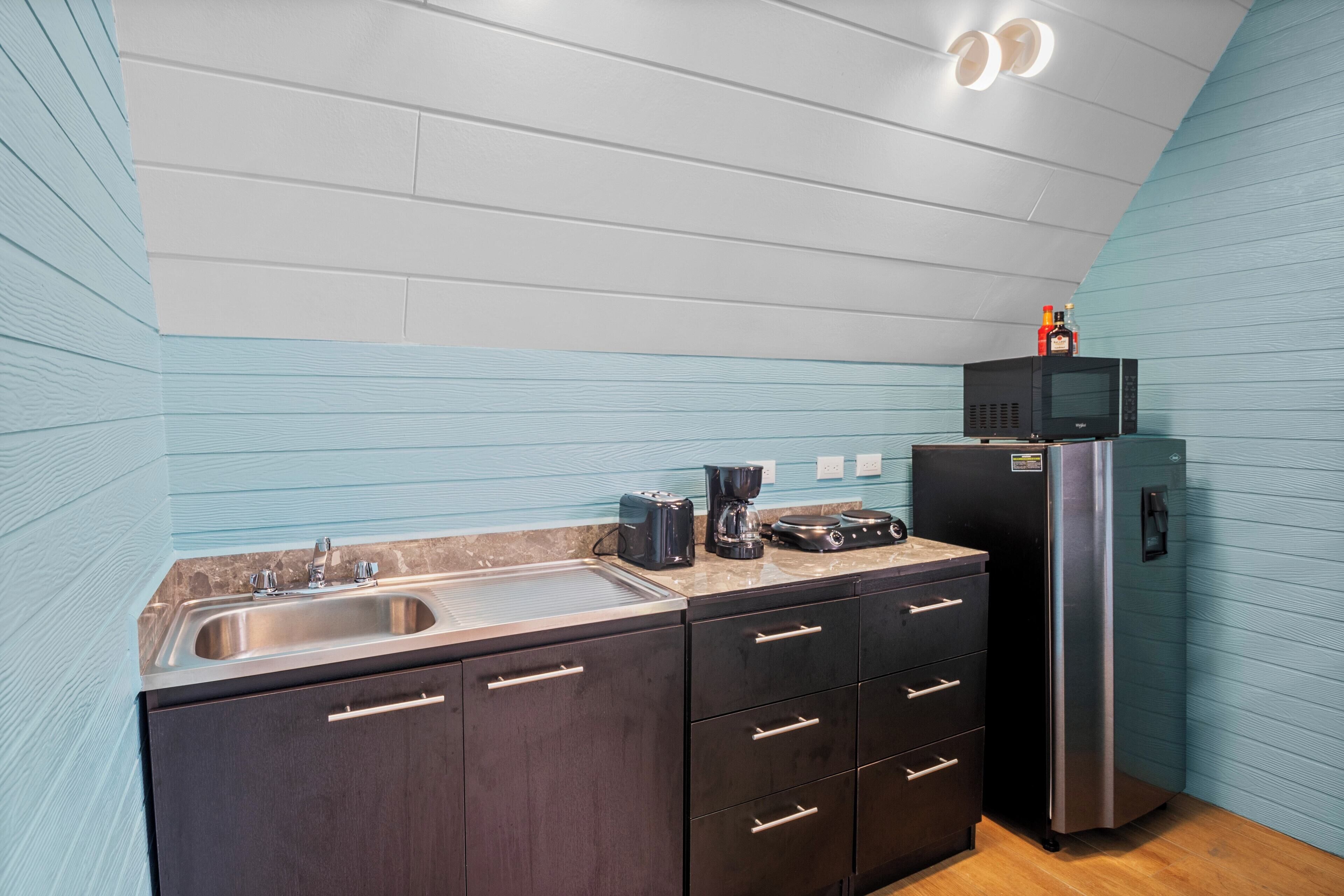 A modern kitchen with a stainless steel sink, dark cabinetry, a black refrigerator, and a microwave on the countertop.
