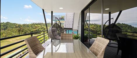 A balcony with wicker furniture, a glass table, and a view of a lush landscape.