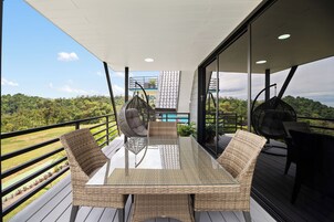 Un balcón con mobiliario de mimbre, una mesa de vidrio y vistas a un paisaje exuberante.