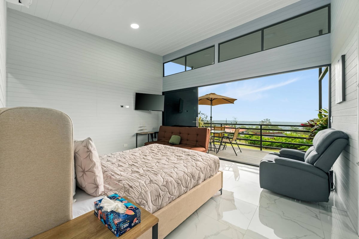 Un dormitorio moderno con cama, sofá, televisor y balcón con vistas.