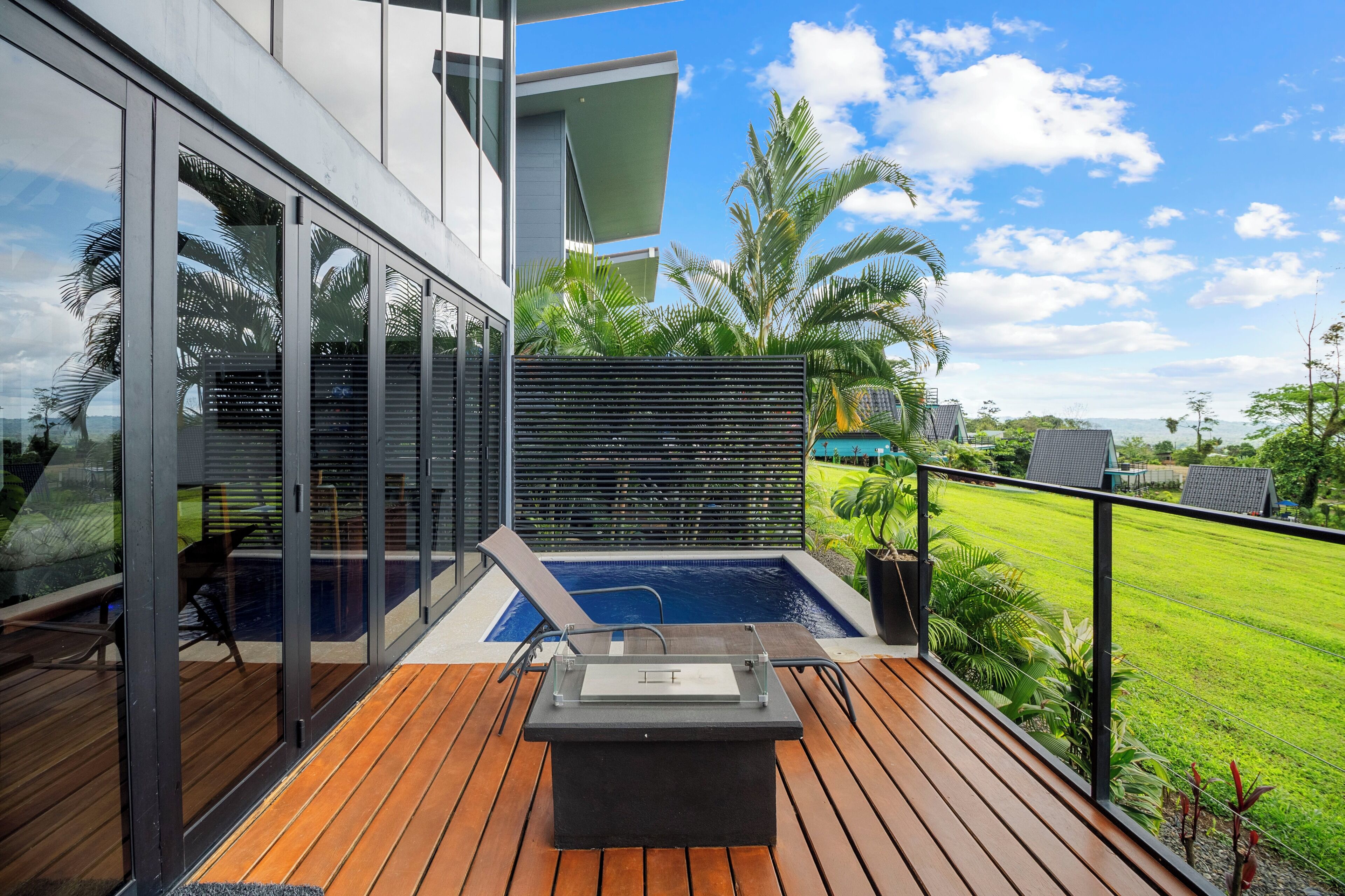 Um deck moderno ao ar livre com hidromassagem, piso de madeira e portas de vidro que dão para uma área de piscina.