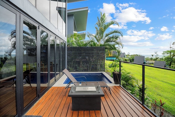 Una terraza moderna al aire libre con un jacuzzi, piso de madera y puertas de vidrio que dan a una zona de piscina.