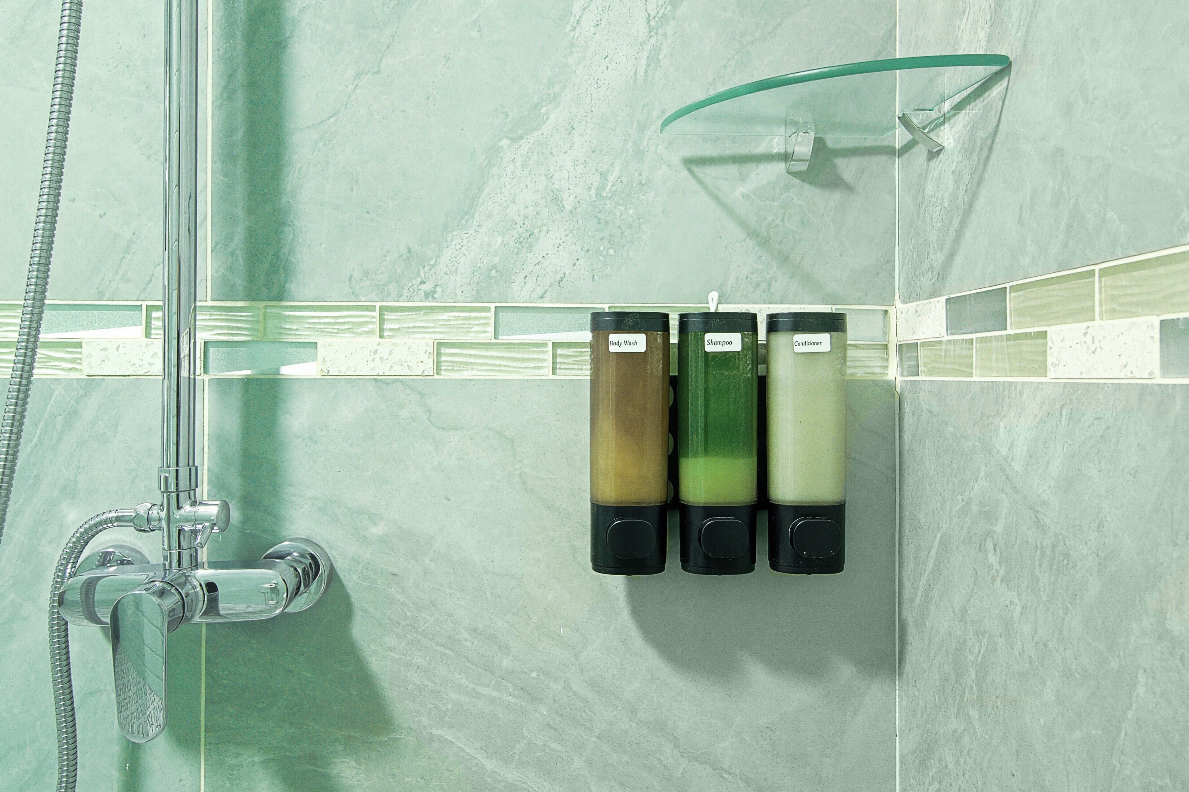 Un baño con ducha, puerta de vidrio y tres botellas de productos para el cuerpo, champú y acondicionador.