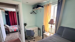 Un dormitorio con cama, escritorio, silla y ventana con cortinas.