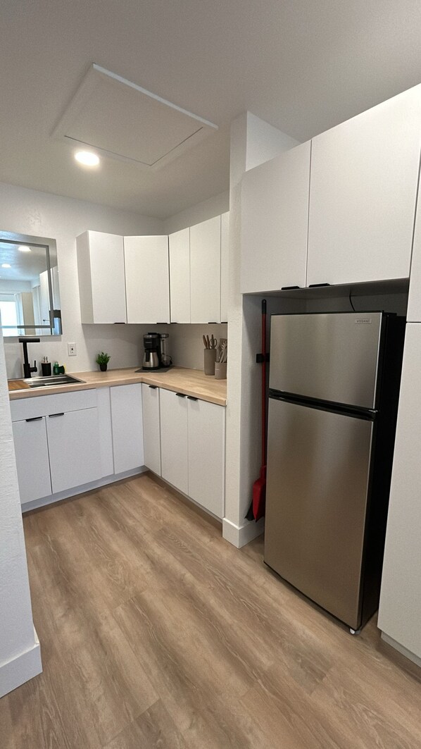 Una cocina moderna con armarios blancos, un refrigerador de acero inoxidable y una encimera de madera.