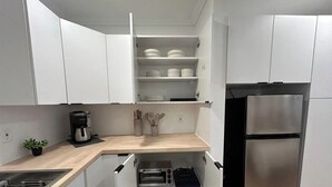Een kleine keuken met witte kastjes, een roestvrijstalen koelkast en een inbouwoven.
