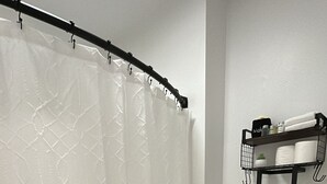 Een badkamer met een witte douchegordijn, een toilet en een plank met handdoeken en toiletartikelen.