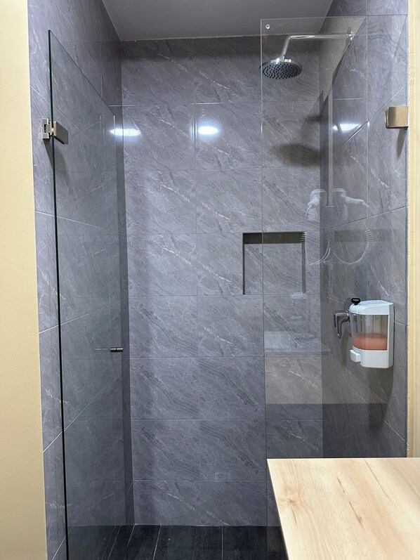 A modern bathroom with a glass-enclosed shower, marble walls, and a wooden vanity. - Amaranto Suites (Medellín)