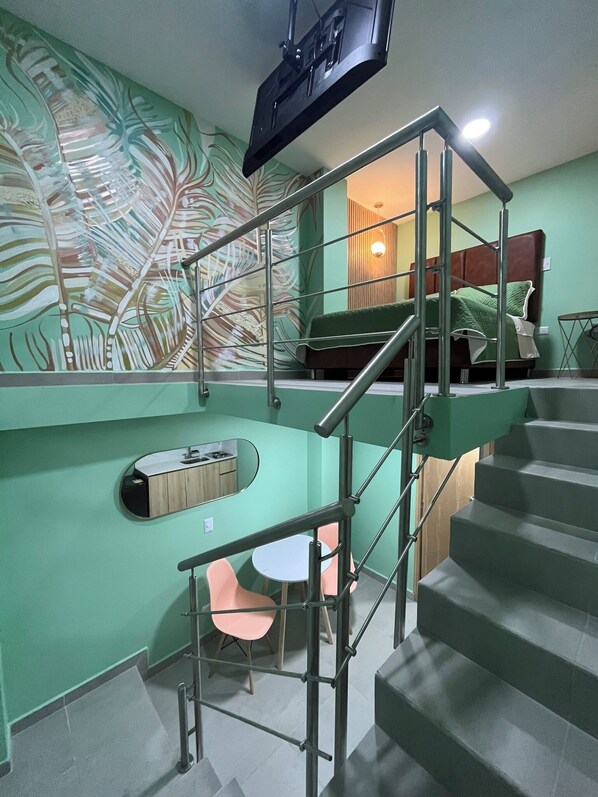 Un interior moderno con una escalera, un pequeño comedor con mesa y sillas, y un gran mural abstracto en la pared.