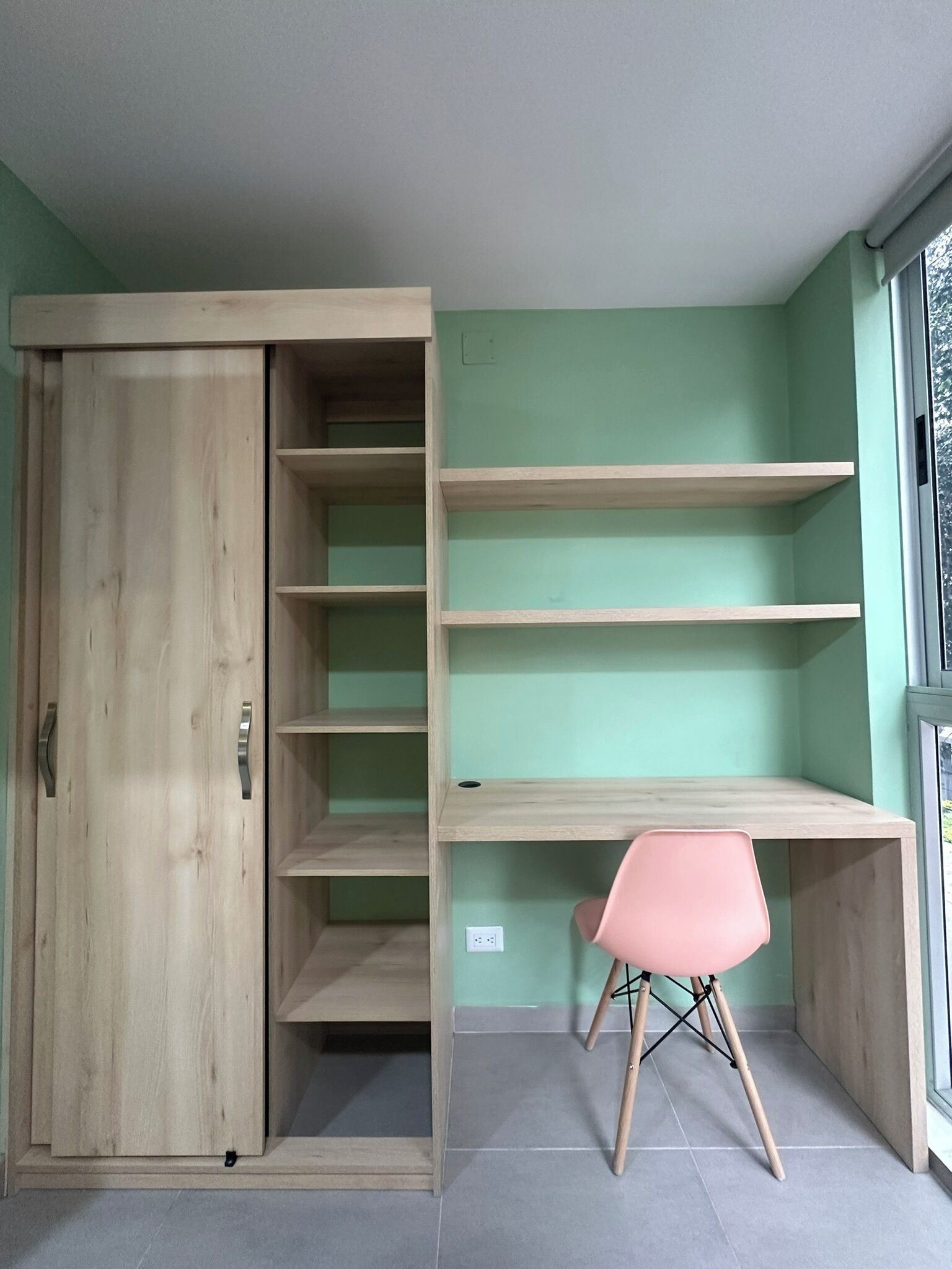 A room with a wooden wardrobe, a pink chair, and built-in shelves.