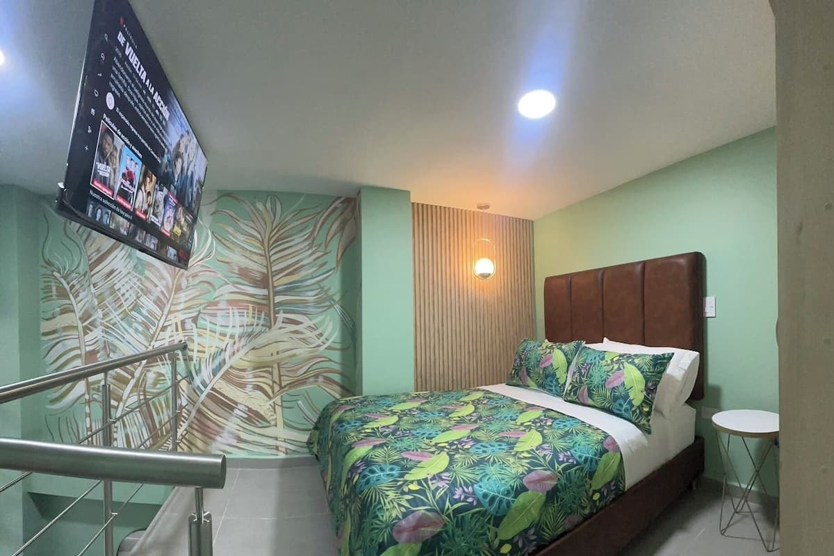 Une chambre d’hôtel avec un lit, une petite table ronde, un téléviseur fixé au mur et un escalier muni d’une rampe.